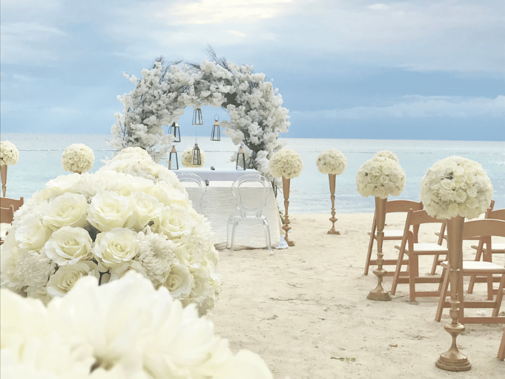 Arco nupcial de playa blanco con flores y faroles para el mar